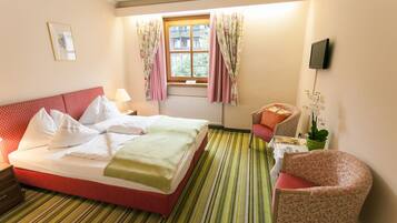 A hotel room with a bed, a chair, a table, a TV, and a window with curtains.