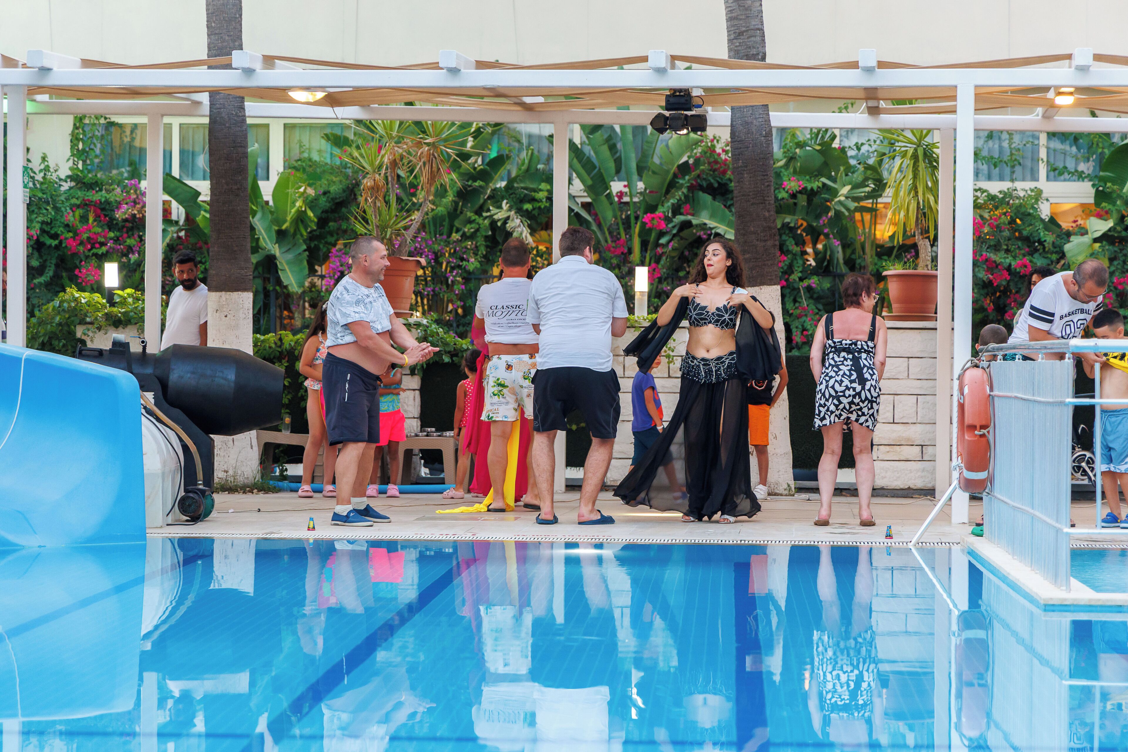 Un área de piscina con superficie de agua cristalina, rodeada por una terraza techada y exuberante vegetación tropical.