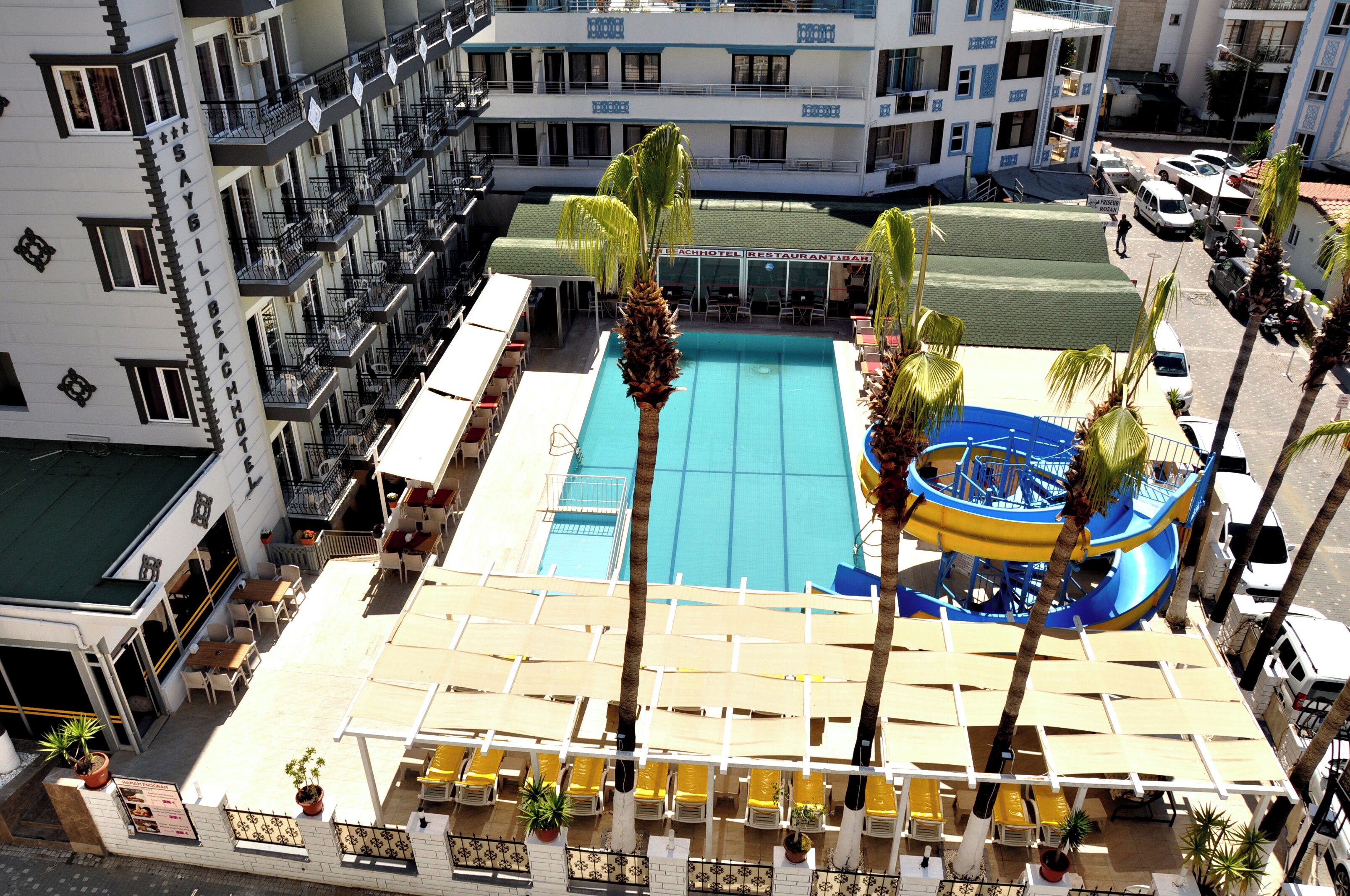 Un espace piscine d’hôtel comprenant un toboggan aquatique, des chaises longues et un bâtiment doté de balcons.