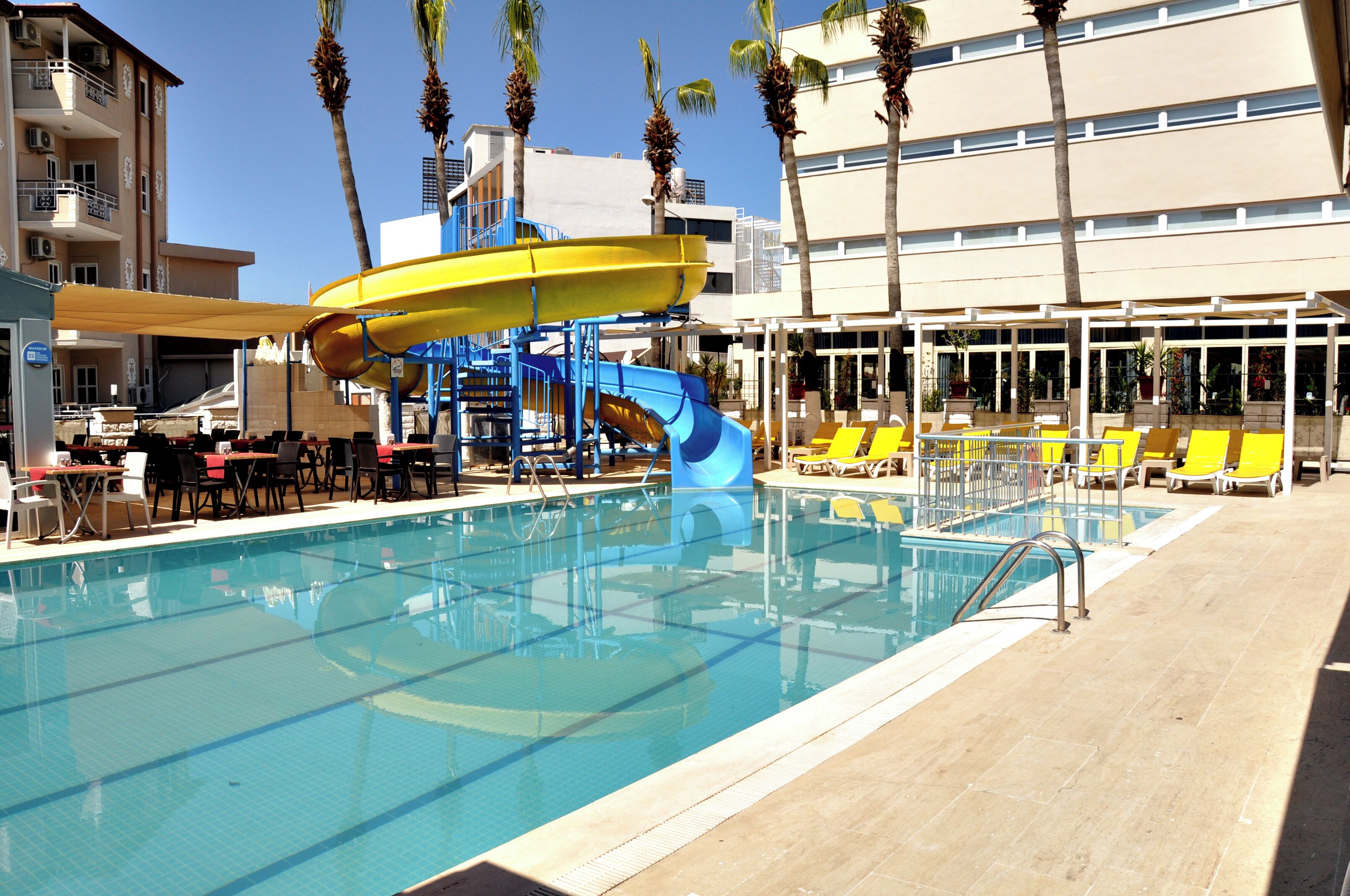 A pool with a water slide, lounge chairs, and a building with balconies.