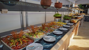 Buffet com diversos pratos, incluindo arroz, legumes e carne, dispostos sobre uma mesa comprida.