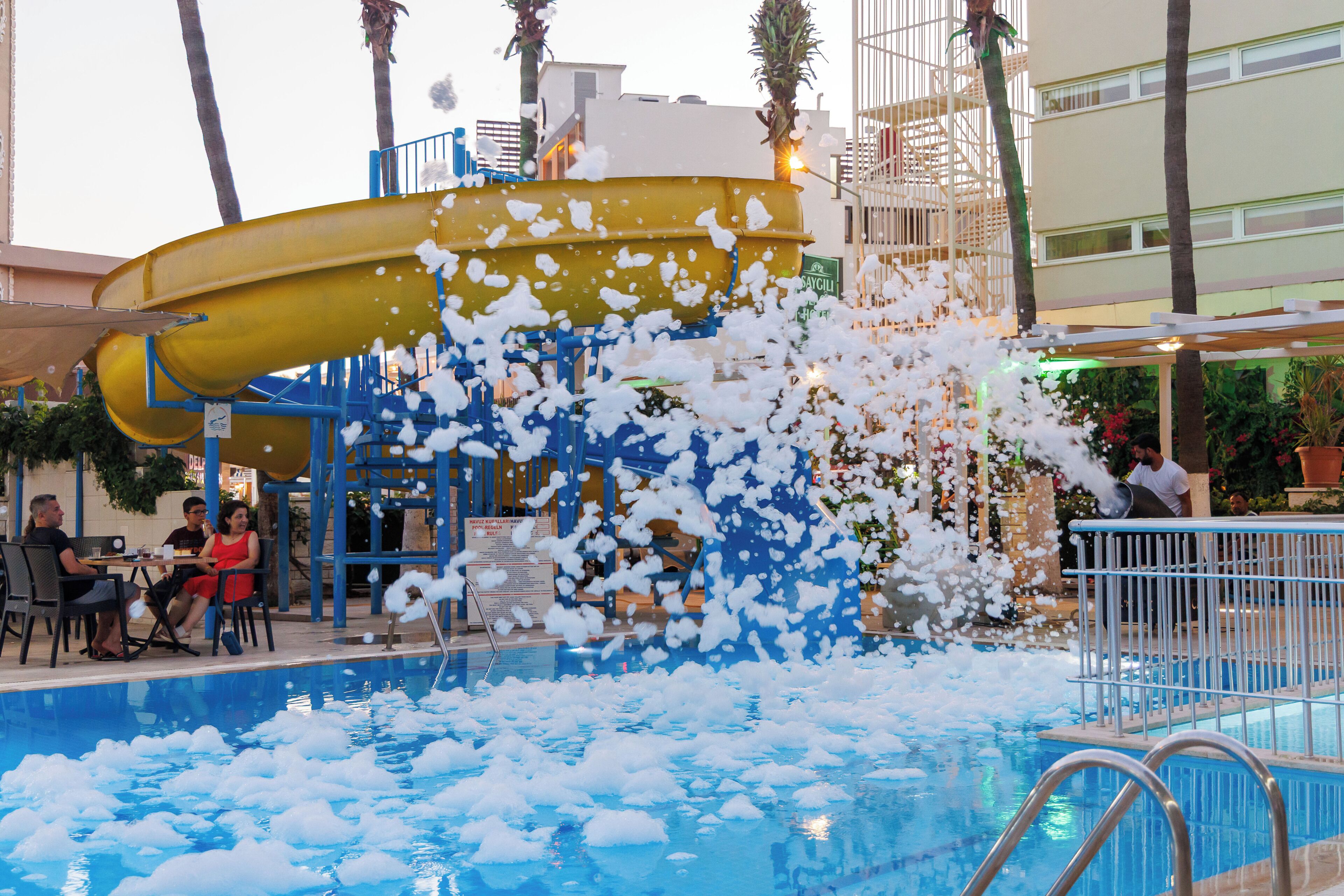 A water slide with foam at the end, a pool, and a seating area with tables and chairs.