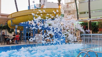 A water slide with foam at the end, a pool, and a seating area with tables and chairs.
