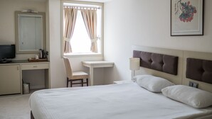 A hotel room with a bed, a desk, a chair, a TV, and a window with curtains. - Palm Inn Hotel (Izmir)