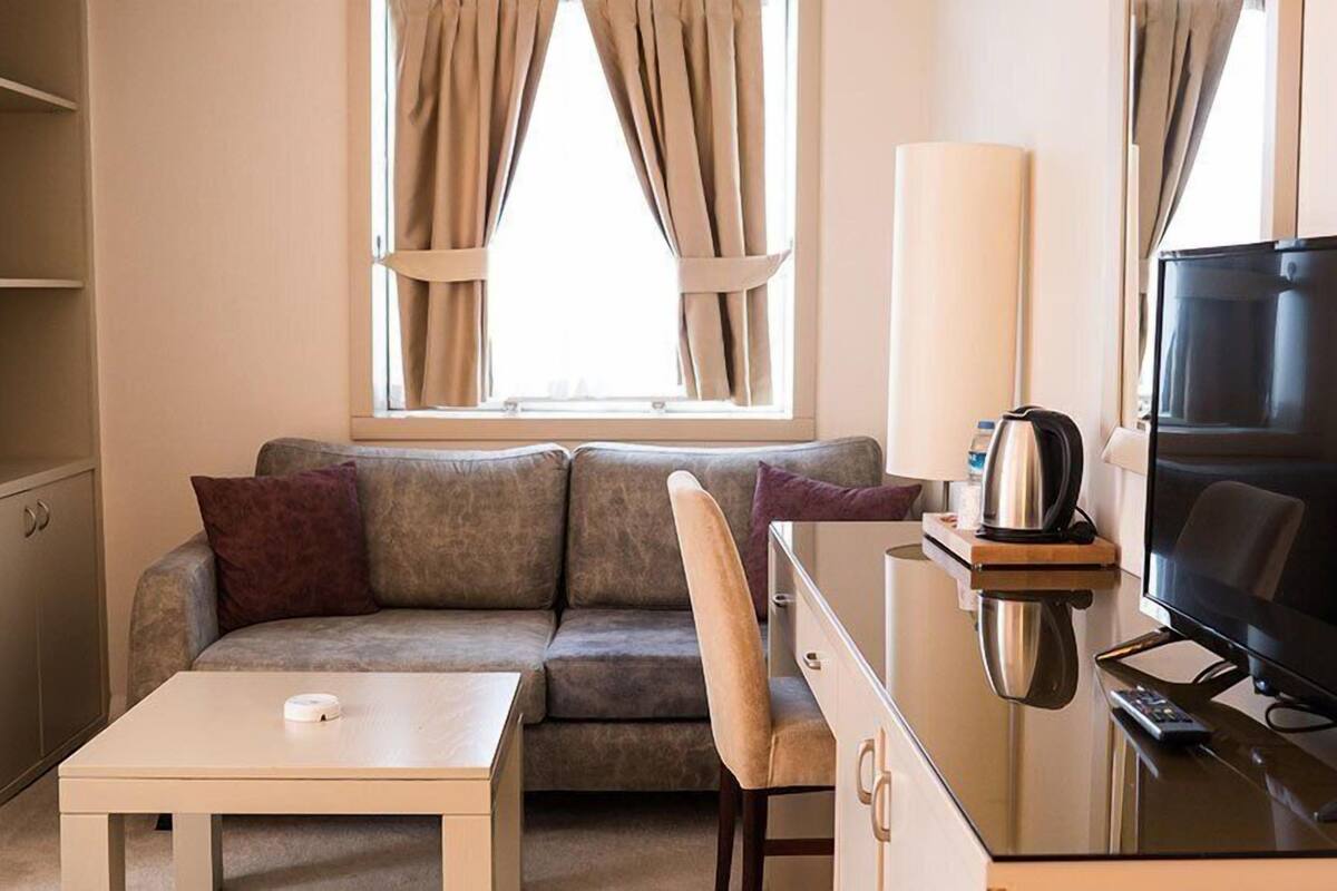 A hotel room with a sofa, a small table, a TV, and a lamp.
