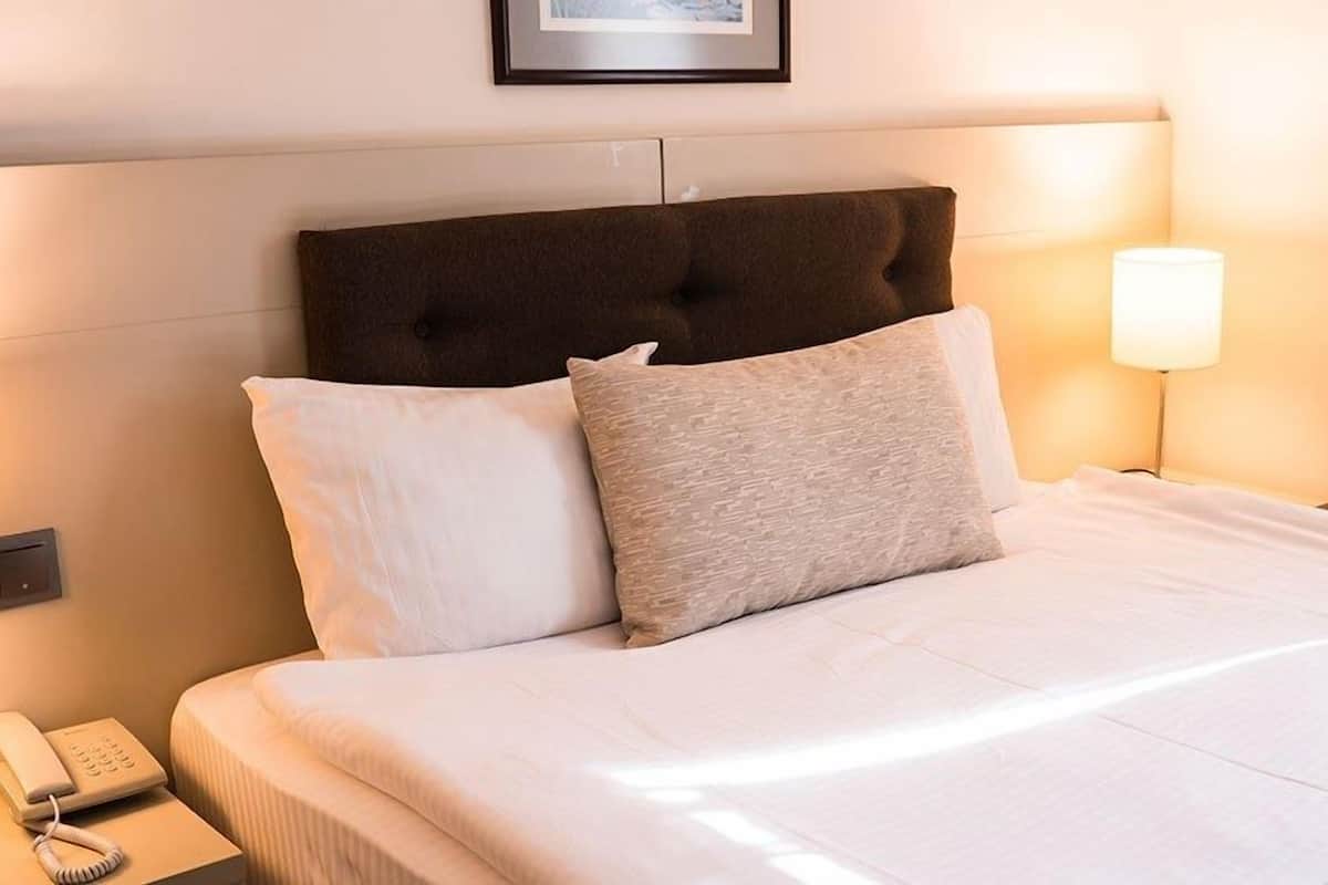 A neatly made bed with a headboard, a bedside lamp, and a telephone on the nightstand.