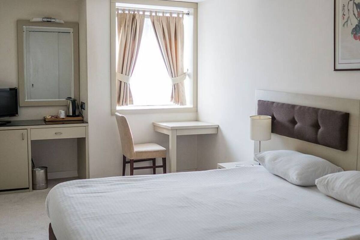 A hotel room with a bed, a desk, a chair, a television, and a window with curtains.