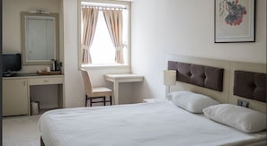 Ett hotellrum med en säng, ett skrivbord, en stol, en tv och ett fönster med gardiner.