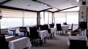 A restaurant with tables and chairs, large windows, and a view of the city. - Palm Inn Hotel (Izmir)