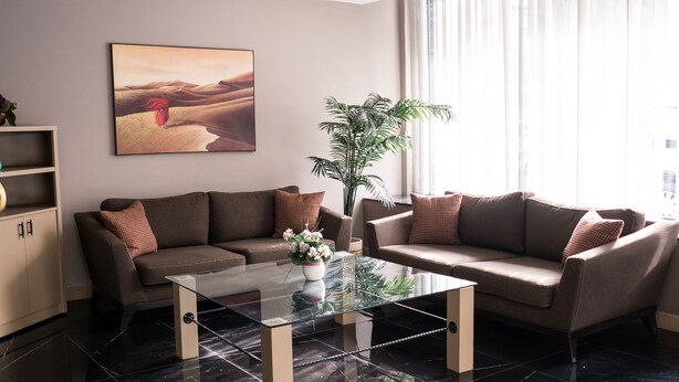 A modern living room with a glass coffee table, two sofas, a large potted plant, and a desert-themed painting on the wall. - Palm Inn Hotel (Izmir)
