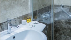 A bathroom with a glass-enclosed shower, a white sink, and a mirror above the sink. - Palm Inn Hotel (Izmir)