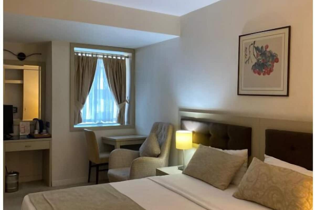 A hotel room with a bed, desk, chair, and a window with curtains.