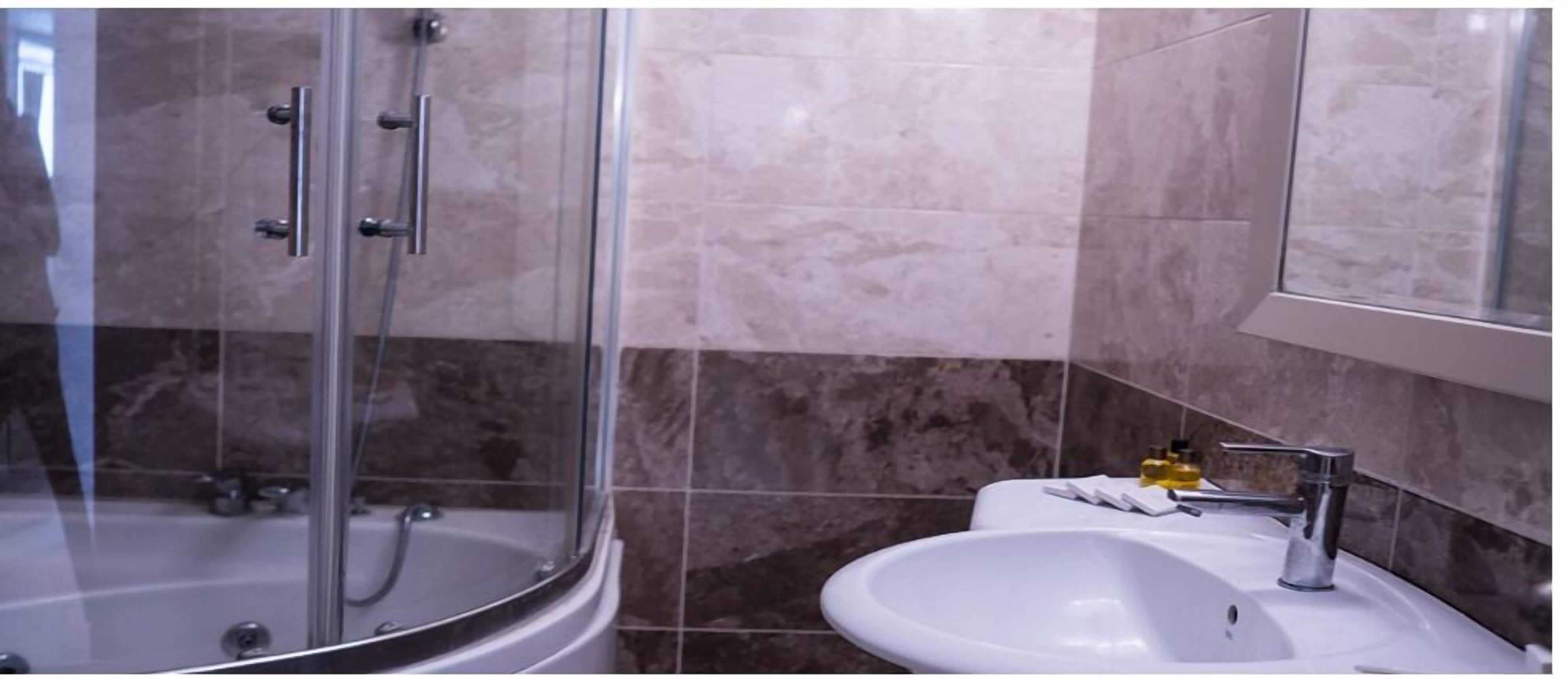 Un bany amb dutxa trencada per vidre, un lavabo blanc i un mirall sobre el lavabo.