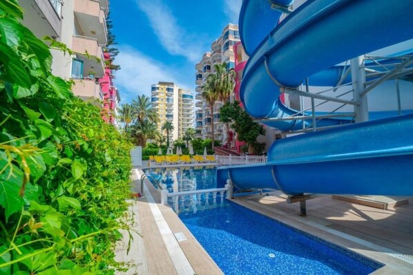 Une piscine avec un toboggan, entourée d’immeubles à plusieurs étages dotés de balcons.