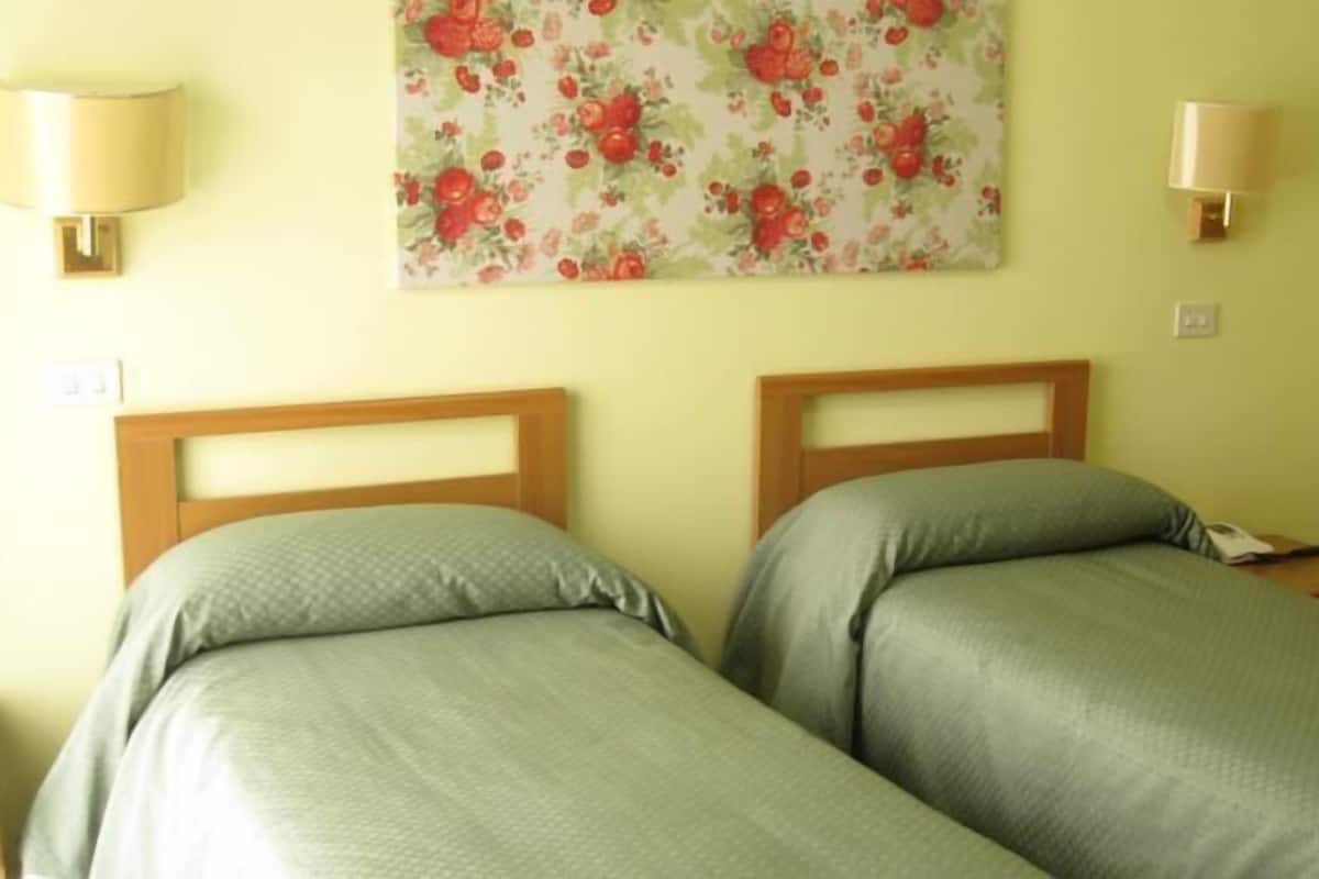 Une chambre avec deux lits simples, une décoration murale à motifs floraux et deux lampes fixées au mur.