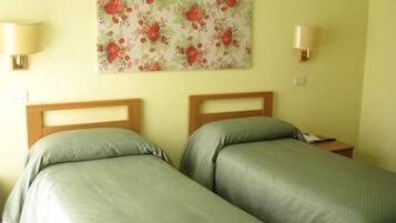 A room with two single beds, a floral wall hanging, and two wall-mounted lamps.