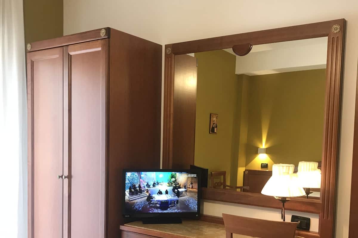 Une chambre d’hôtel avec un bureau en bois, une télévision, une chaise et un grand miroir.