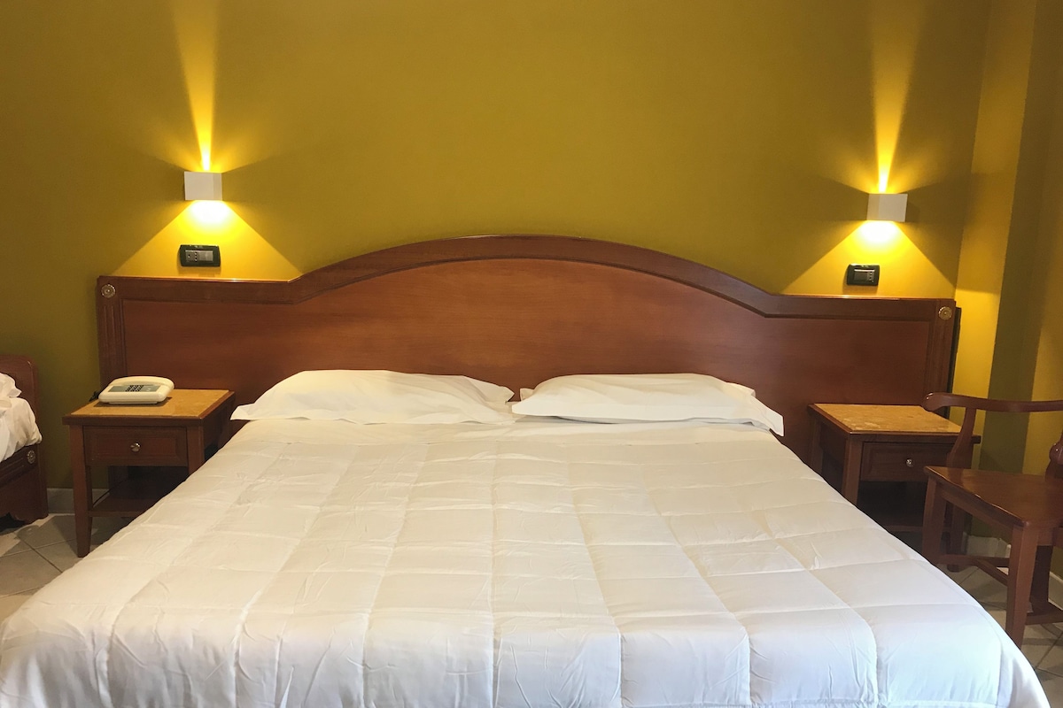 Un lit bien fait, avec une tête de lit en bois, deux tables de chevet avec des lampes et un téléphone posé sur l’une des tables.