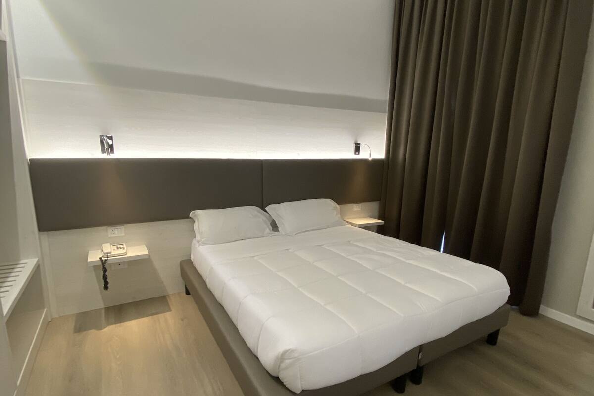 Une chambre d’hôtel moderne avec un grand lit, des tables de chevet et une petite table intégrée servant de table de nuit.