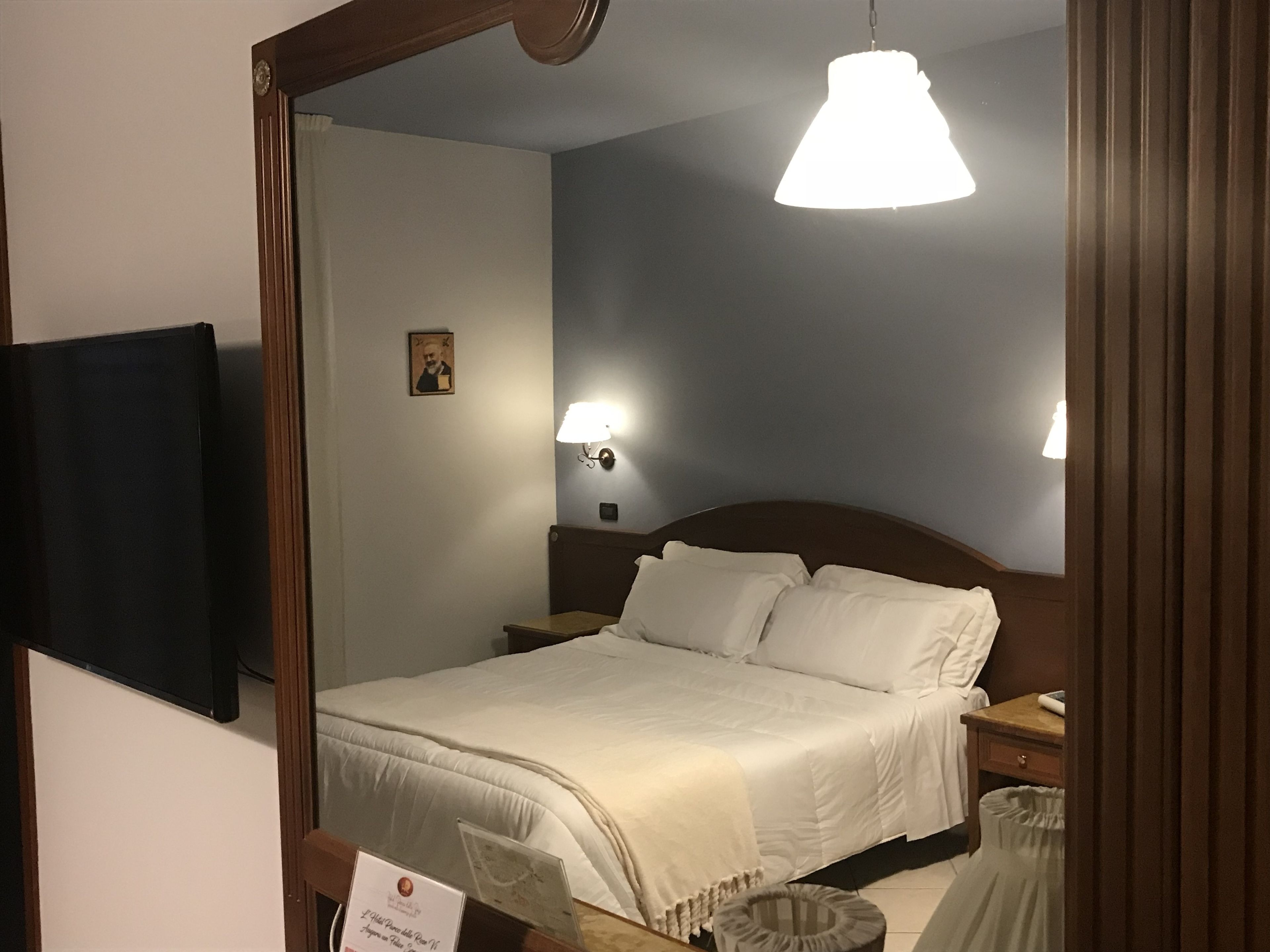 A hotel room with a large bed, two bedside tables, a nightstand, a wall-mounted TV, and a ceiling light fixture.