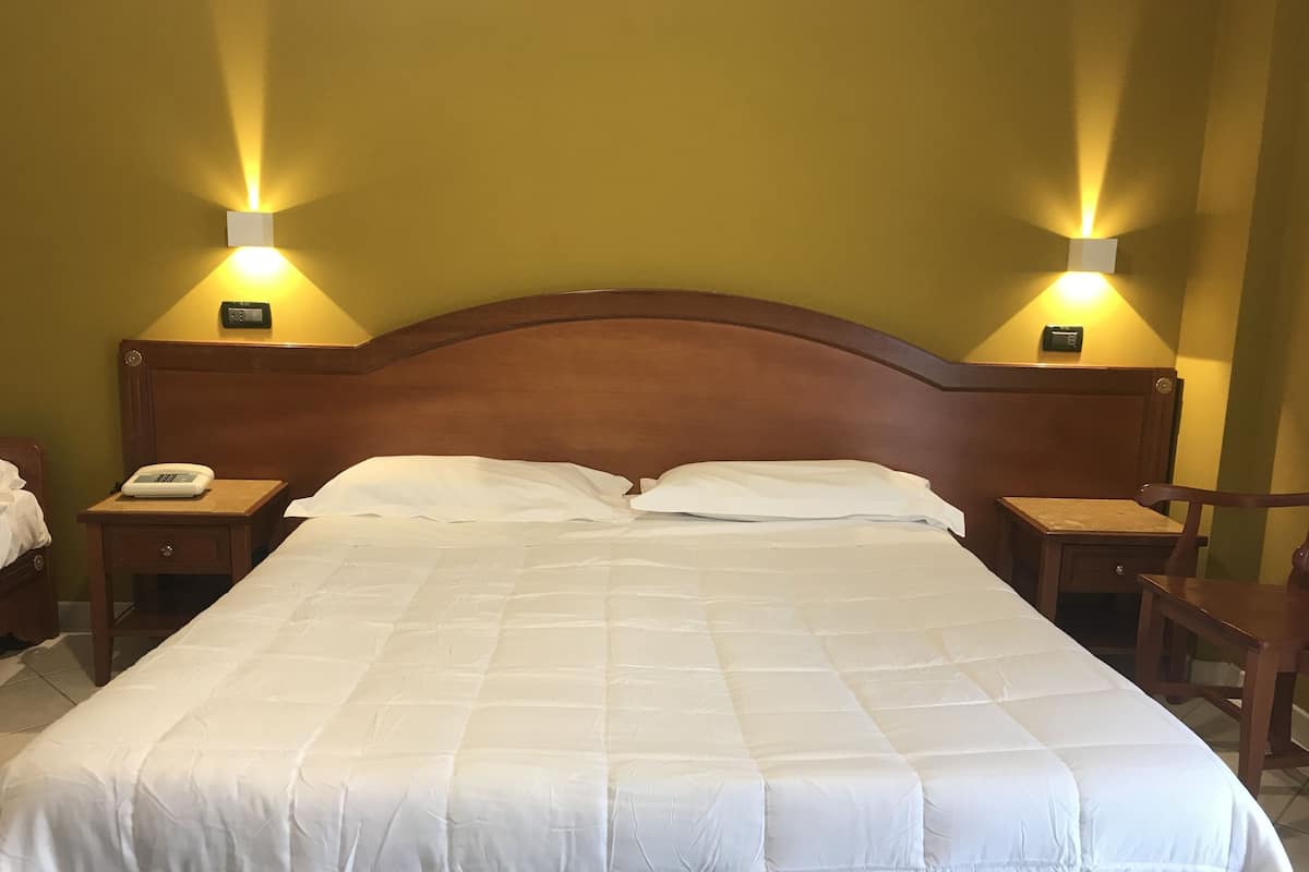 Un lit bien fait, avec une tête de lit en bois, deux tables de chevet avec des lampes et un téléphone sur l’une des tables.