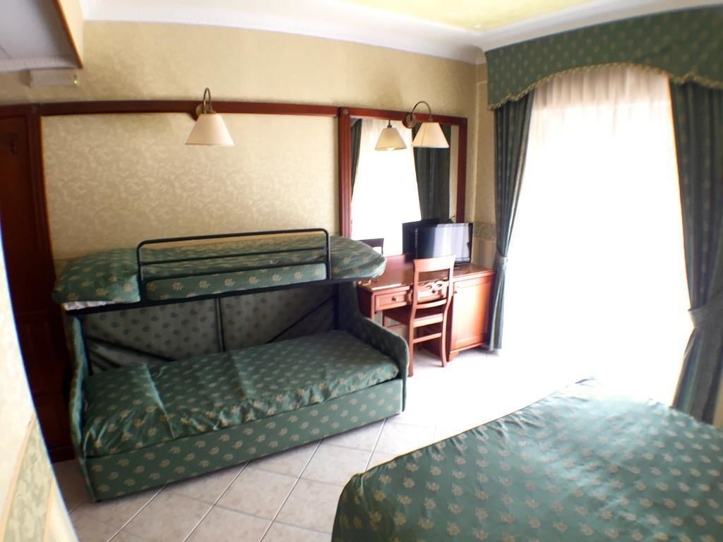 A room with bunk beds, a desk with a television, and curtains.