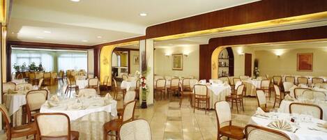 A spacious dining area with multiple round tables, each set with white tablecloths and chairs.