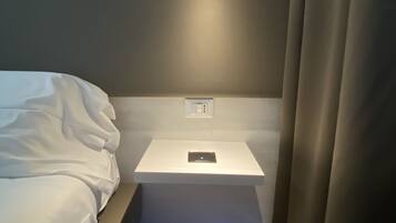 A modern hotel room with a bed, bedside table, and a wall-mounted light fixture.