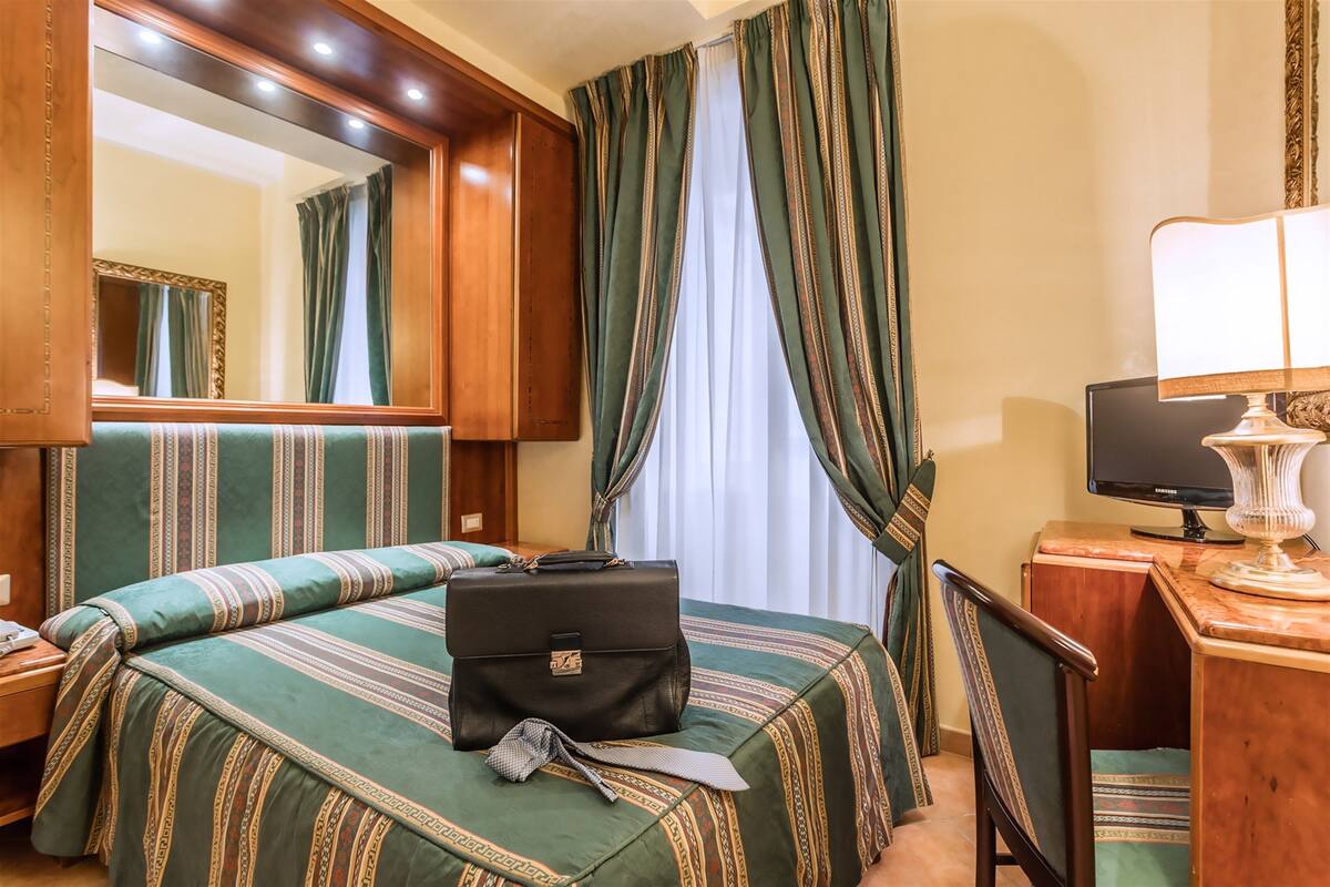 A hotel room with a large bed, a desk with a lamp, a television, and a mirror.