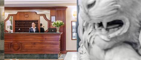 A reception desk with a wooden finish, a marble floor, and a statue in the foreground.