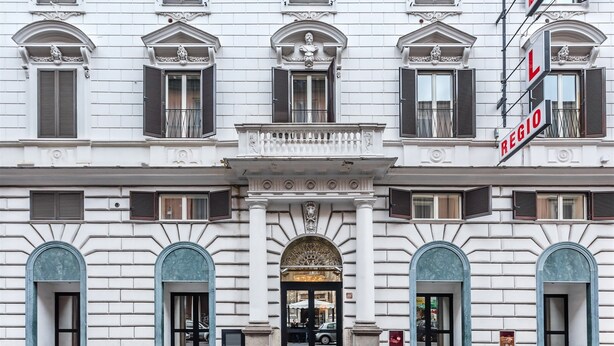 A hotel facade with a classical architectural style, featuring symmetrical windows, decorative moldings, and a prominent entrance with a grand archway. - Raeli Hotel Regio (Rome)