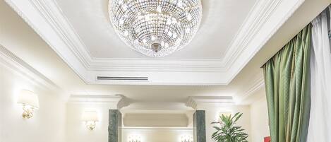 Un hall d’entrée luxueux, agrémenté d’un imposant lustre, de canapés à rayures, d’un sol en marbre et d’un grand miroir.