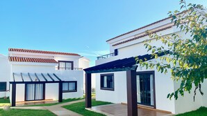A modern two-story house with a patio, a covered outdoor seating area, and a well-maintained lawn. - Aparthotel Nuramar (Ciutadella de Menorca)
