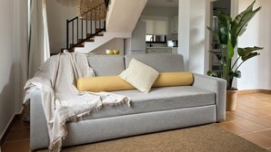 A living room with a grey sofa, a yellow pillow, a white throw blanket, and a large green plant. - Aparthotel Nuramar (Ciutadella de Menorca)