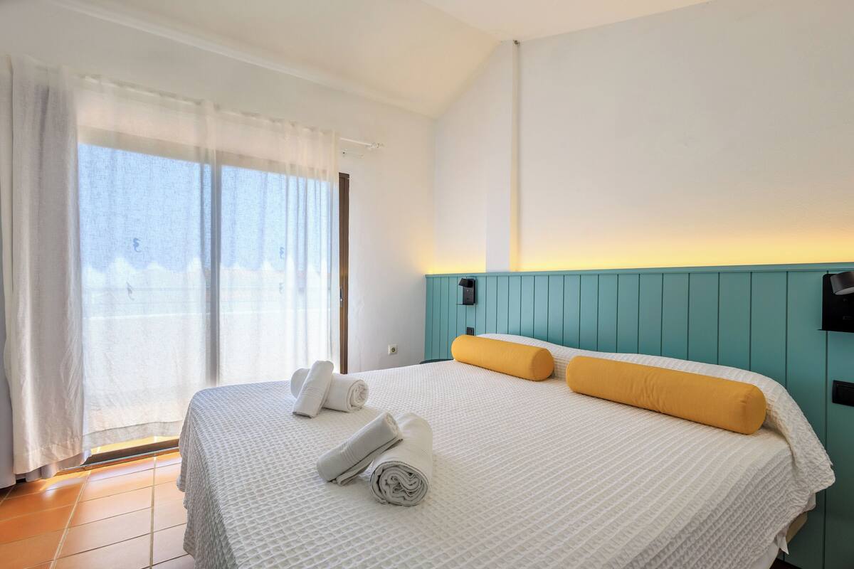 Ein Hotelzimmer mit Bett, einem fenster mit Vorhängen und einer Wandleuchte.