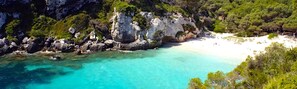 Eine Küstenlandschaft mit klarem türkisblauem Wasser, felsigen Klippen und einem Sandstrand.
