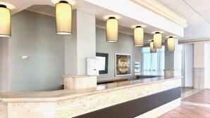 A reception desk with a marble top, multiple pendant lights, a framed sign, and a water dispenser. - Aparthotel Nuramar (Ciutadella de Menorca)