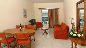 Una sala de estar con una mesa de comedor, sillas, un sofá, un televisor y un balcón con vistas.