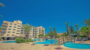 Un área de piscina de hotel con varias piscinas, palmeras y un puente de madera.