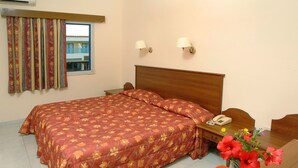 Una habitación de hotel con una cama grande, una mesita de noche con teléfono y un jarrón con flores.