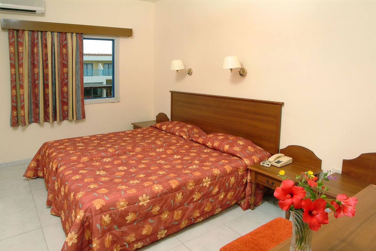 Une chambre d’hôtel avec un grand lit, une table de chevet avec un téléphone et un vase rempli de fleurs.