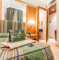 A hotel room with a bed, a bedside table, a lamp, a telephone, and a door.