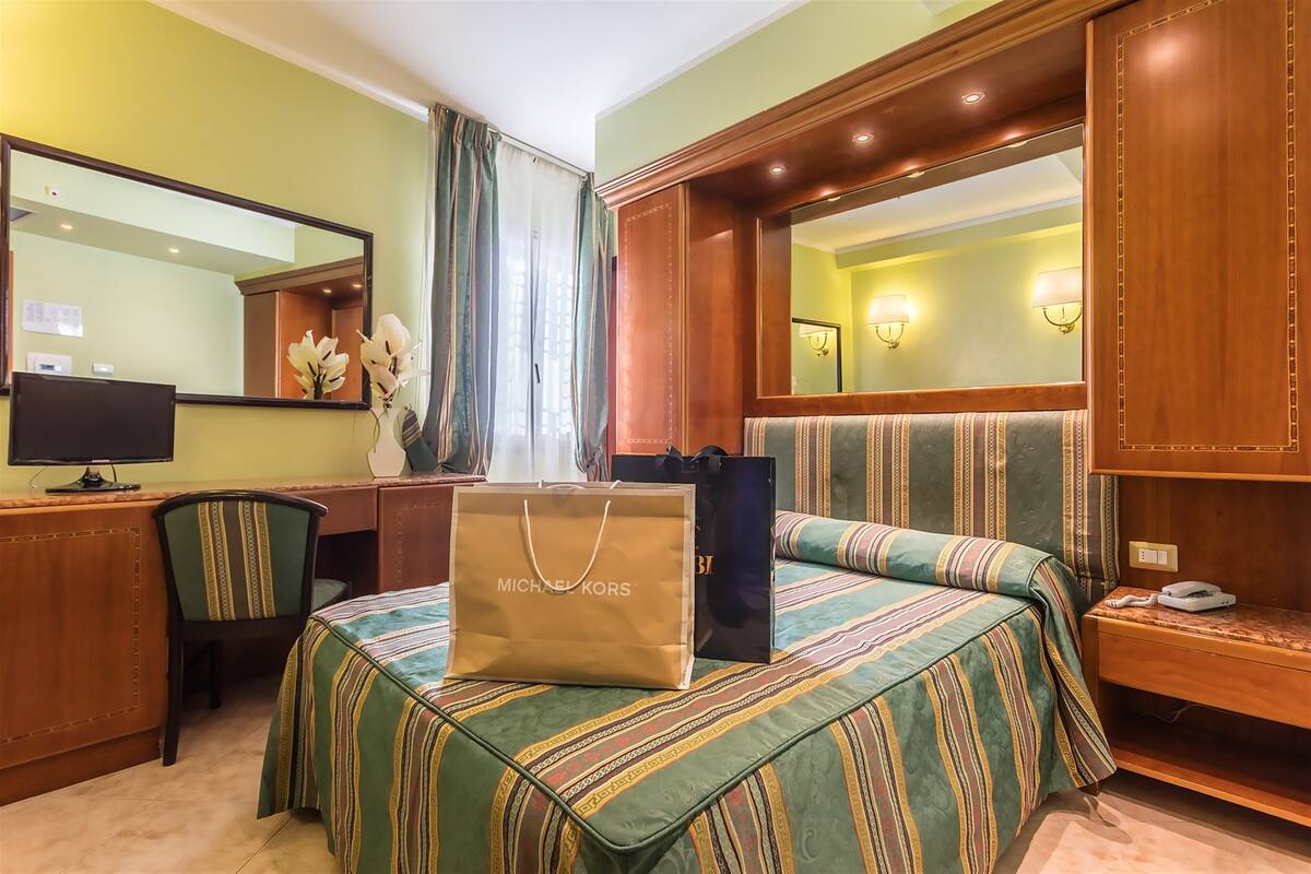 Une chambre d’hôtel comprenant un lit, un bureau, une chaise, un grand miroir et une coiffeuse avec un miroir.