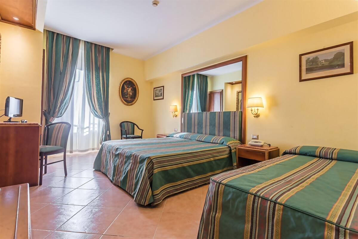 Une chambre d’hôtel avec deux lits, un bureau avec un ordinateur, une chaise et une fenêtre avec des rideaux.