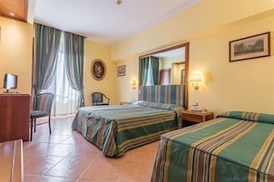 A hotel room with two beds, a desk with a computer, a chair, and a window with curtains.
