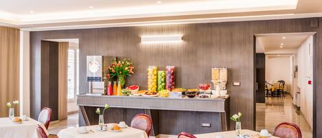 Un comedor de hotel con mesas dispuestas para el desayuno, un bufé con diferentes opciones de comida y un diseño interior moderno.