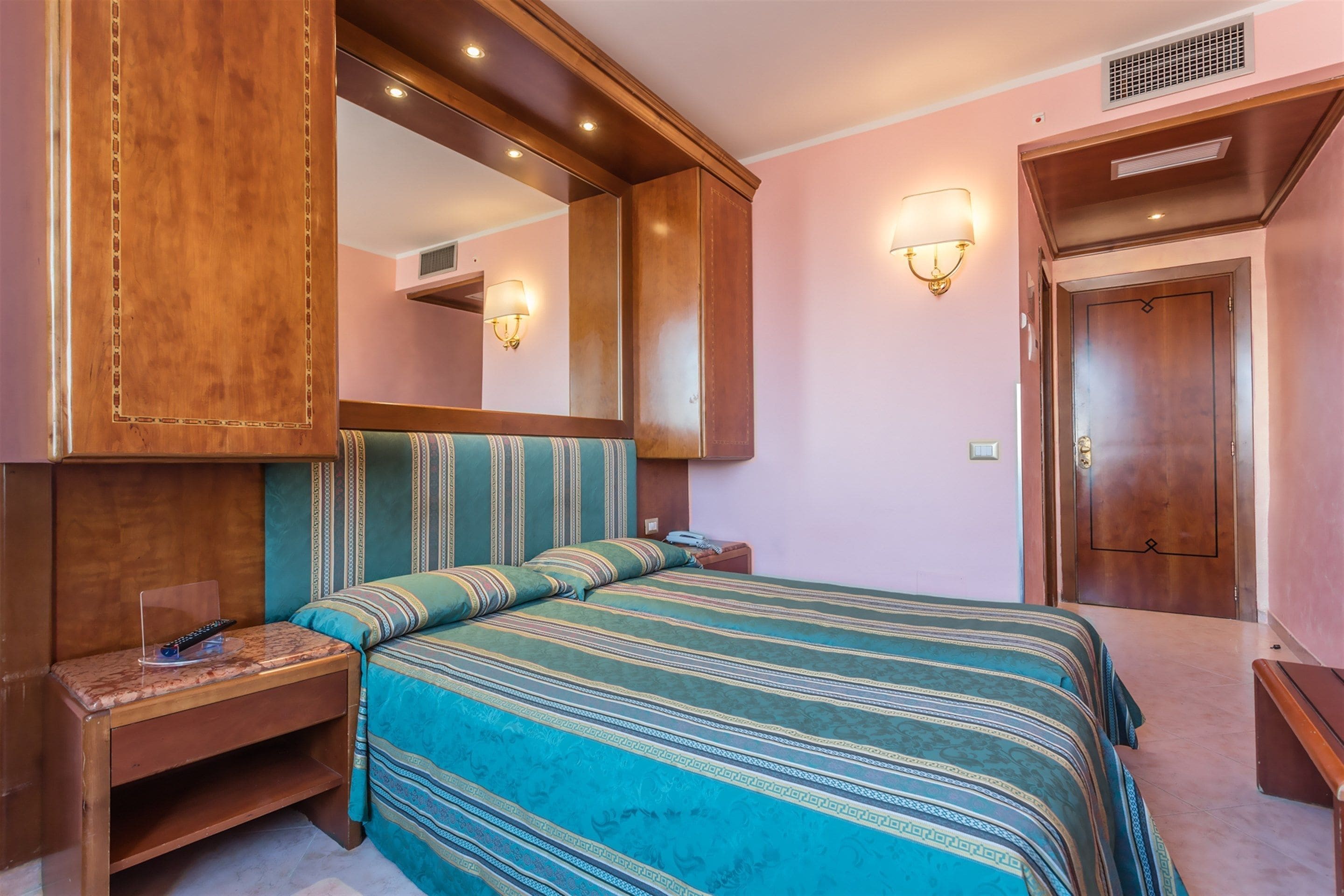 A hotel room with a large bed, a nightstand, a mirror, and a door.