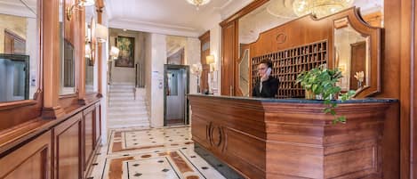 A grand lobby with a marble floor, wooden reception desk, and a large chandelier.