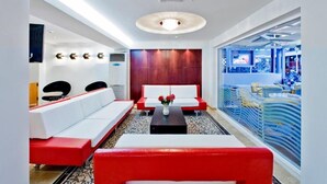 A modern hotel lobby with a red and white sofa set, a coffee table with flowers, and a large window with a view of the city. - Ambassador (Rhodes)