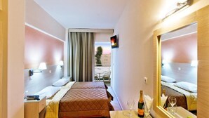 A hotel room with two beds, a large mirror, a small table with a bottle and glasses, and a view of the outside balcony. - Ambassador (Rhodes)